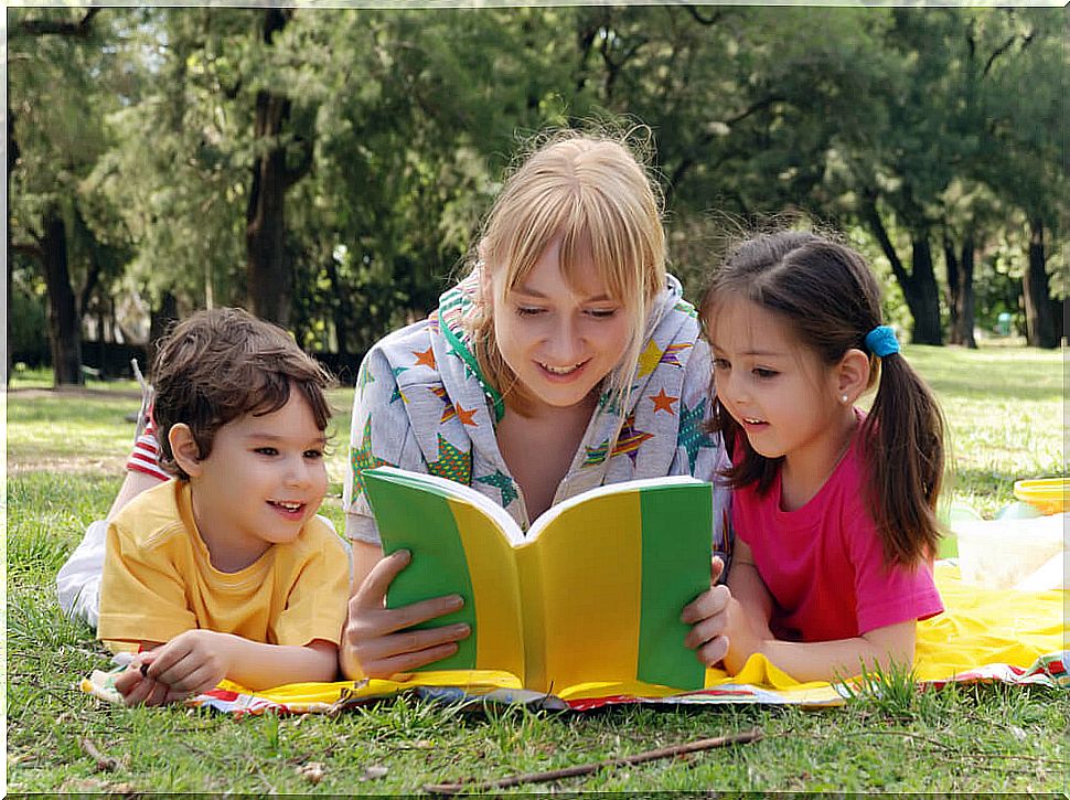 A mother reads a book about emotions to her son and daughter.  They are all three lying in a park.