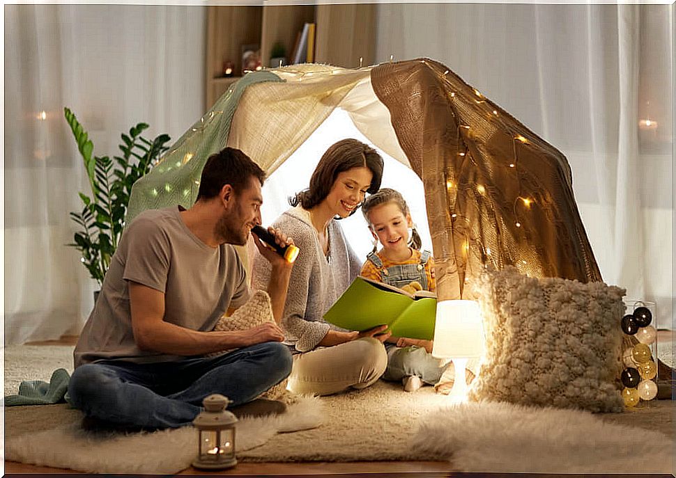 Parents reading with their daughter in a cabin built in the living room at home.