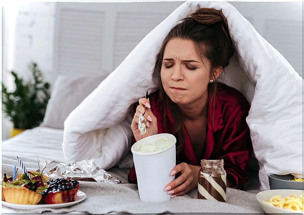 Woman eating ice cream and sweets in bed due to emotional eating.