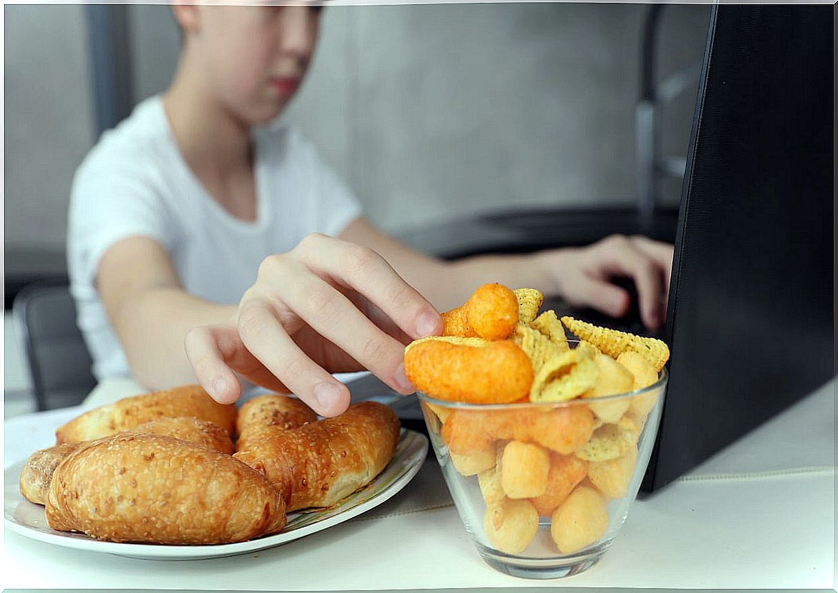 Child eating ultra-processed food while playing computer games.