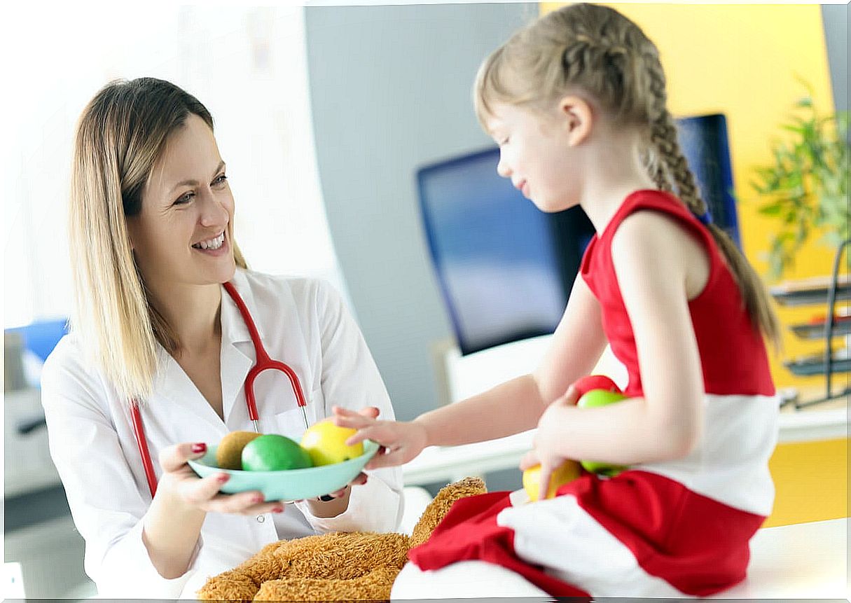 Little girl at the doctor while offering her to eat fruit.