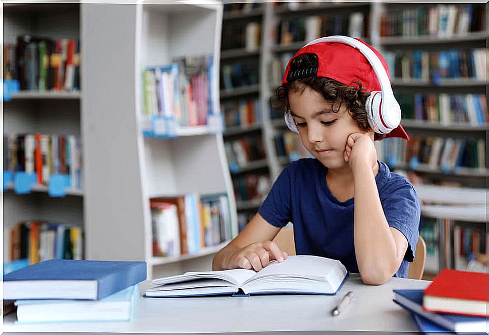 Boy reading a book in the library with headphones on.