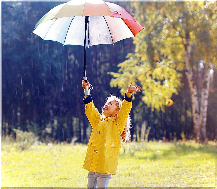 Girl enjoying in the rain with an umbrella and a raincoat.